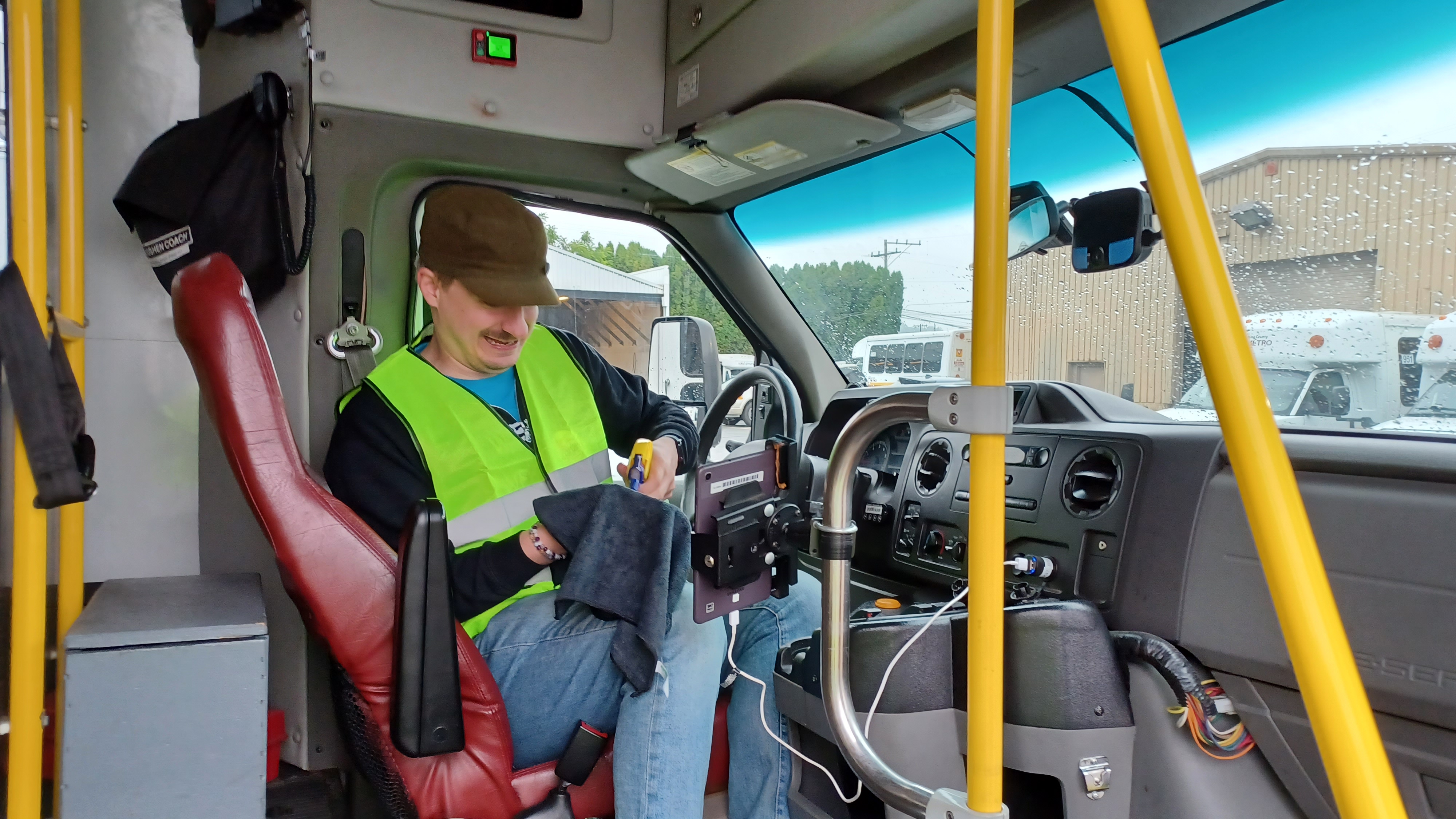 A man sitting in the driver's seat of paratransit bus cleans the drivers area