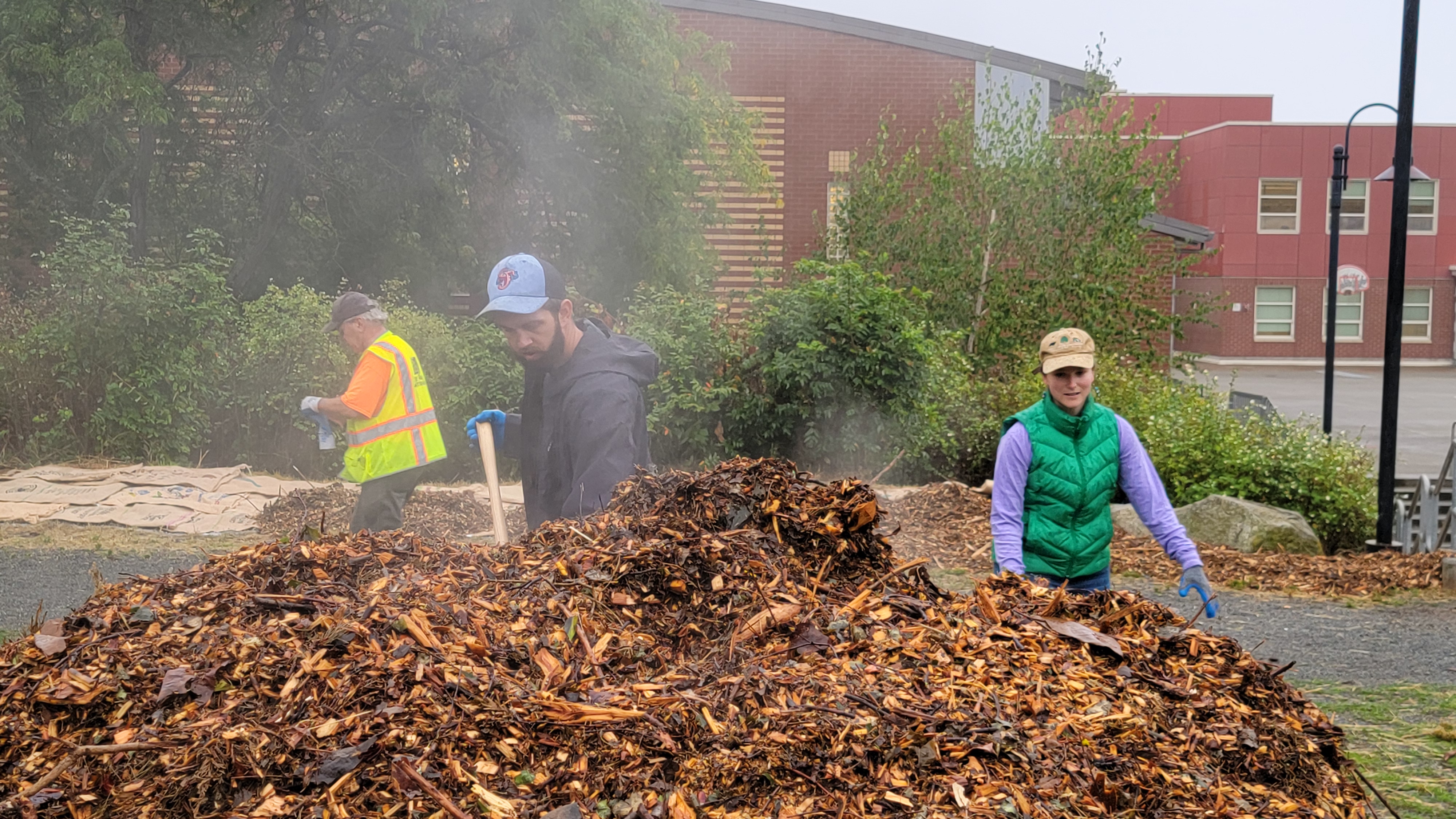 Three people shovel much from large steaming piles