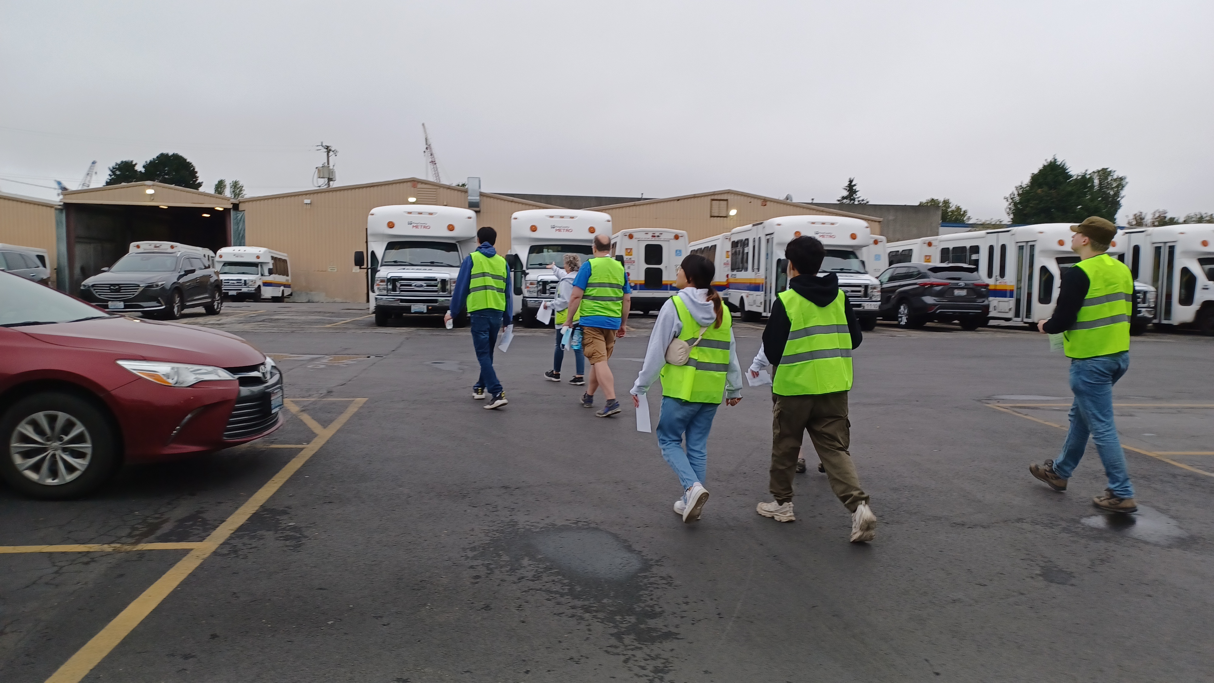 A group of people in neon-yellow vests walk across a parking lot toward several parked buses.