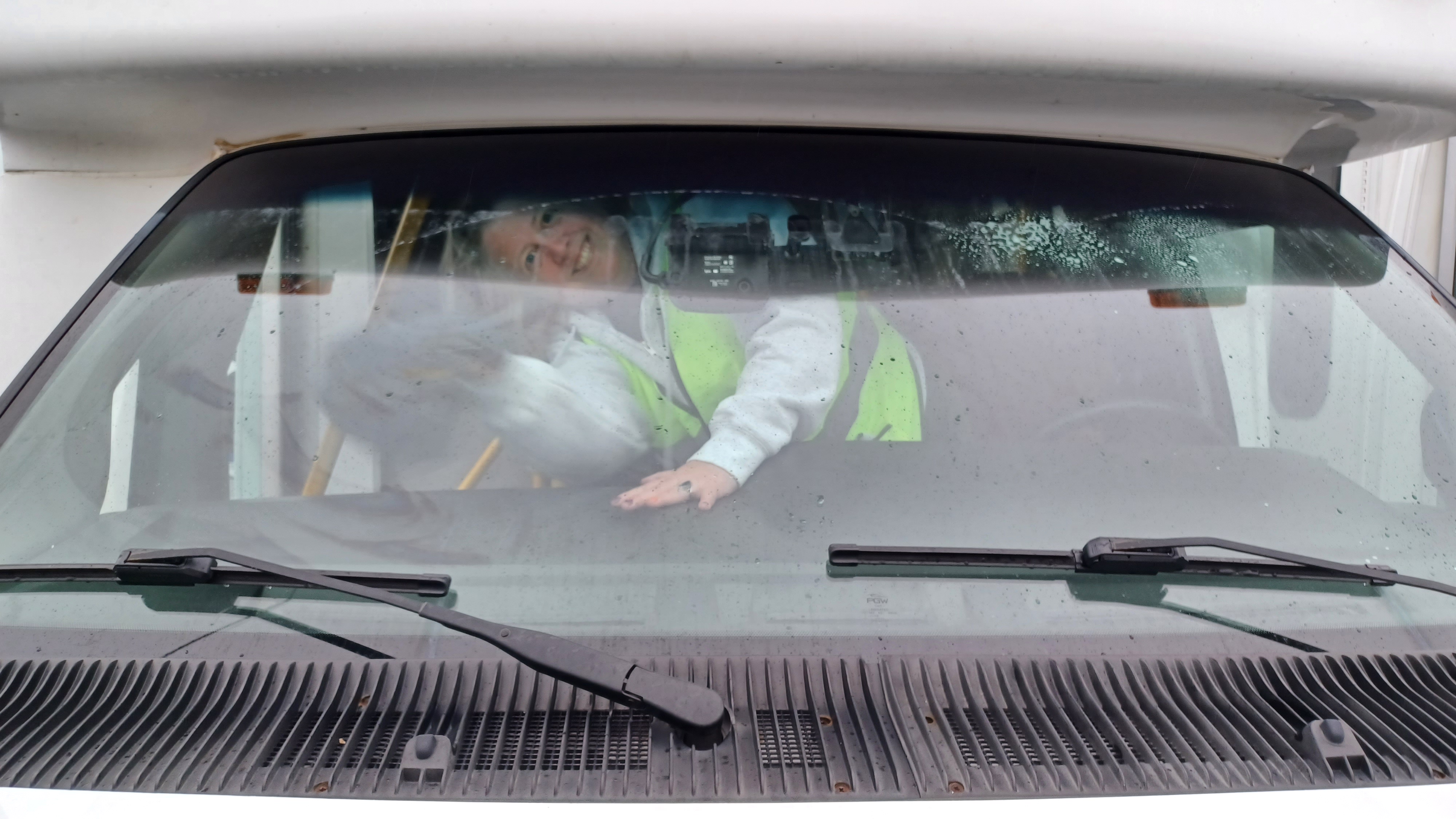 Person smile as she cleans the inside windshield of a white van.