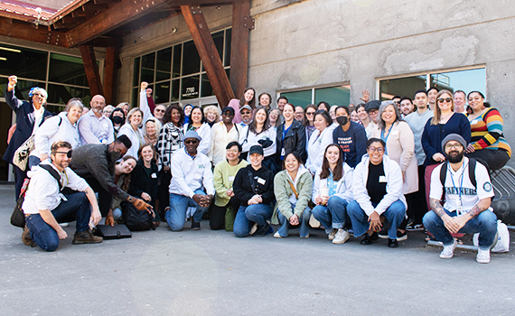 Large group of Solid Ground staff smiling and posing outside a building on a concrete floor.