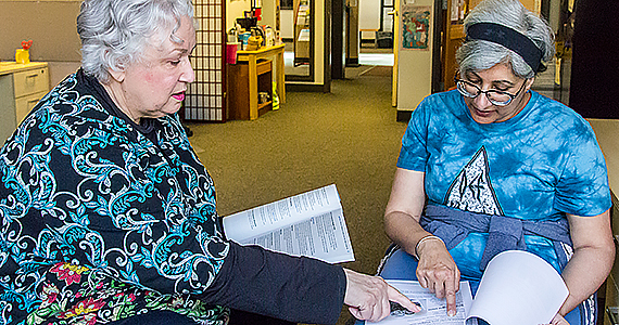 Two gray-haired women holding Medicare materials while discussing them.