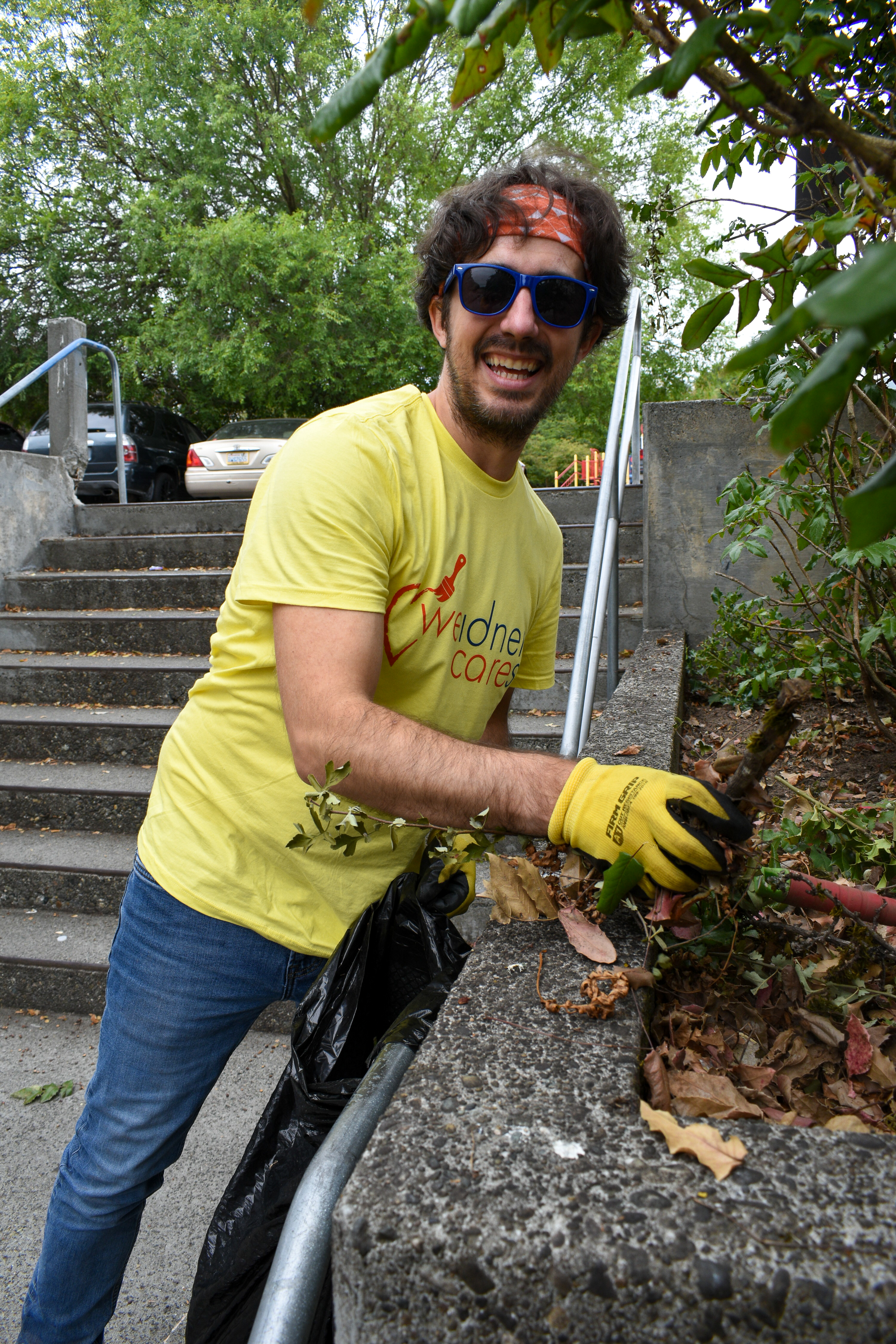 A man in a yellow shirt, jeans, and sunglasses smiles as he works near a cement staircase washer.