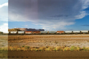 Photo of a long freight train with multi-colored cars in the distance across a grass field.