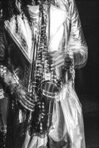 Blurry black and white portrait of a saxophone player, with just the sax and his hands and torso in view.