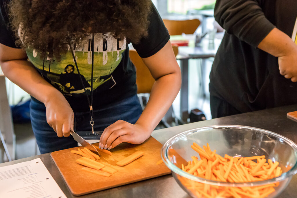 A cooking class student carefully juliennes carrots.