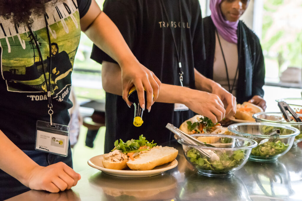 A close up of hands assembling bahn mi sandwiches.