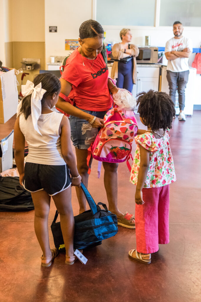 A mother examines a backpack as her kids look on.