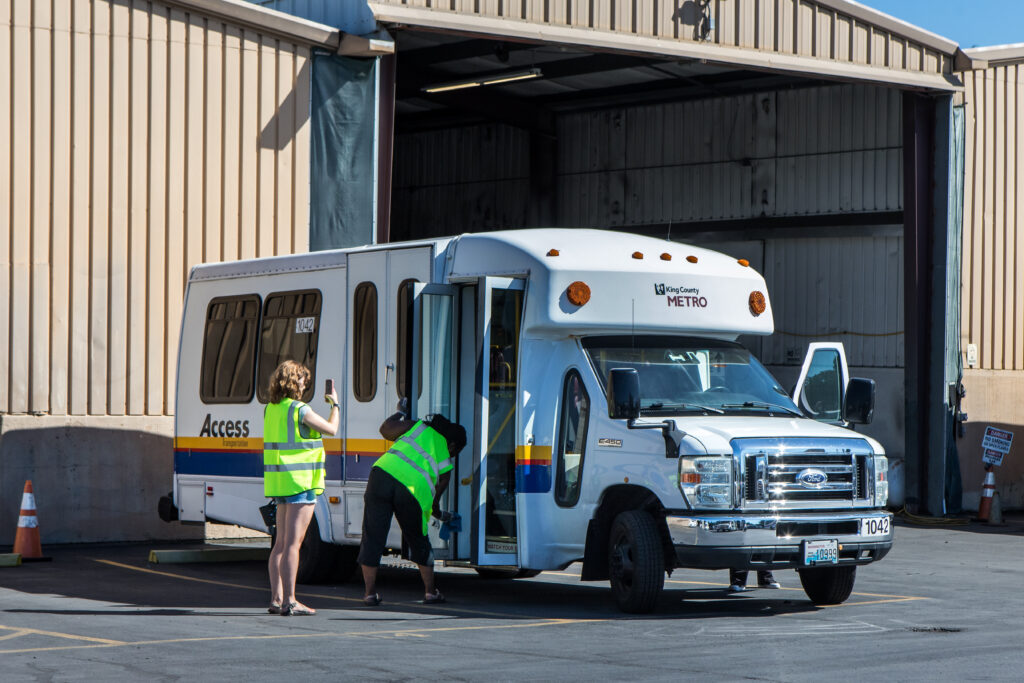 Two people in yellow vests stand outside a paratransit bus.