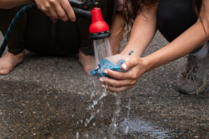 A bunched-up blue cloth is held out in two hands while someone else sprays it with a hose.