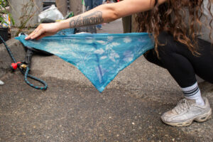 A triangle of blue cloth is outstretched in someone's hands over pavement.