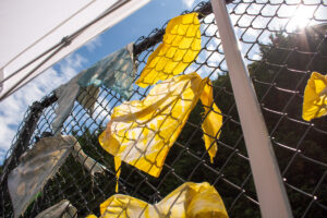 Yellow tie-dyed cloths hang on a chain-link fence.