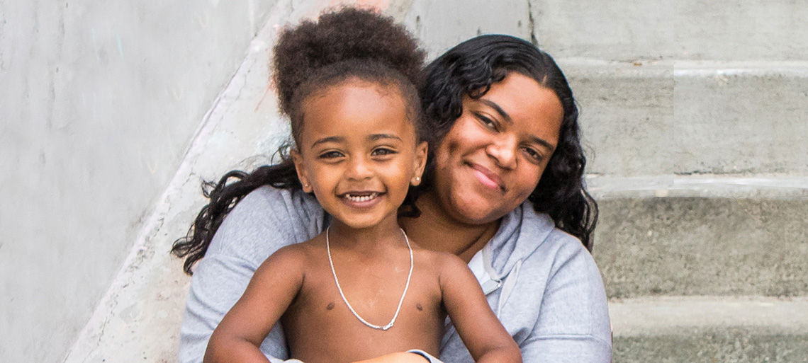 A smiling mother and son pose sitting on concrete steps