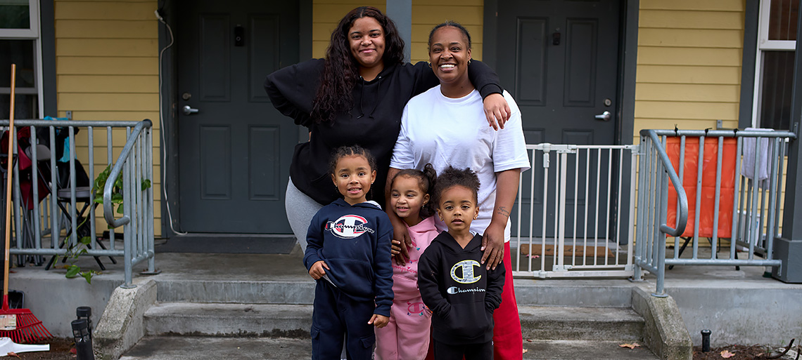Two neighbor moms and their 3 small children pose together in front of their shared front porch.