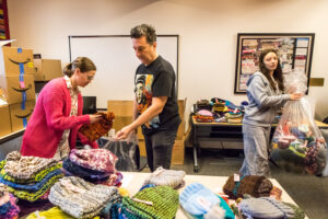 Two young women and an older man sort and bag knitted items.